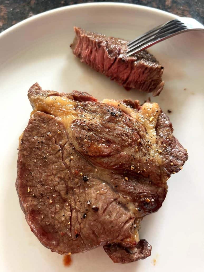 Sliced air fried Delmonico steak on a plate with a fork holding a juicy, medium-cooked bite.