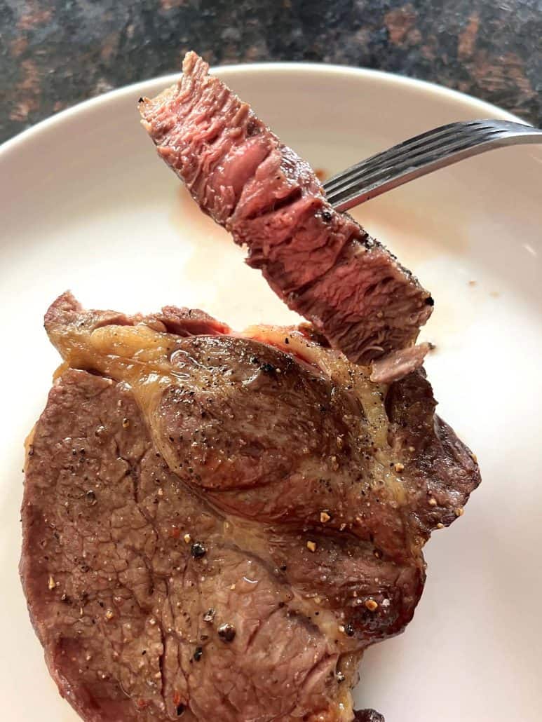 Close-up of a fork holding a juicy, medium-cooked bite of air fried Delmonico steak, showing tender pink center and browned crust.