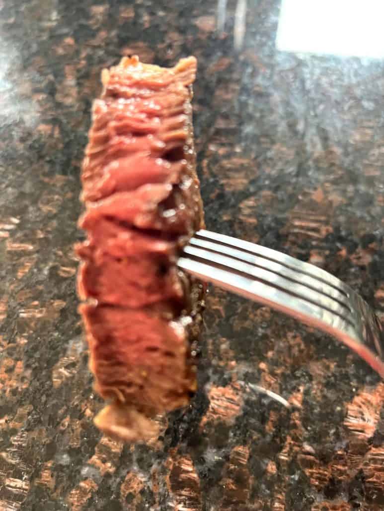 Fork holding a juicy slice of medium-cooked Delmonico steak, showing a perfectly pink center and seared edge.