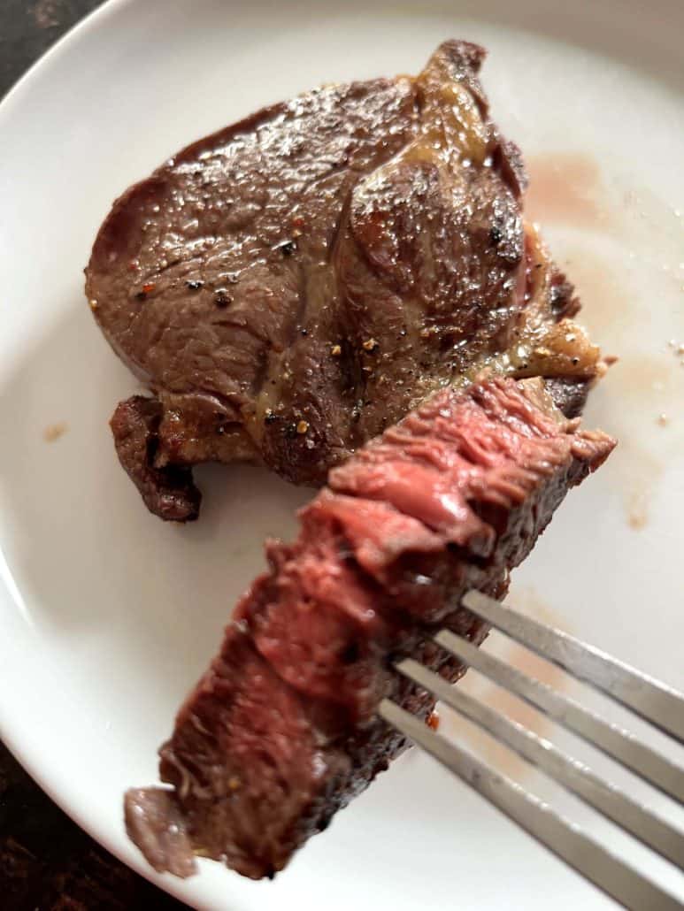 Fork holding a tender slice of air fried Delmonico steak with a pink center, served on a white plate for a perfect medium finish.