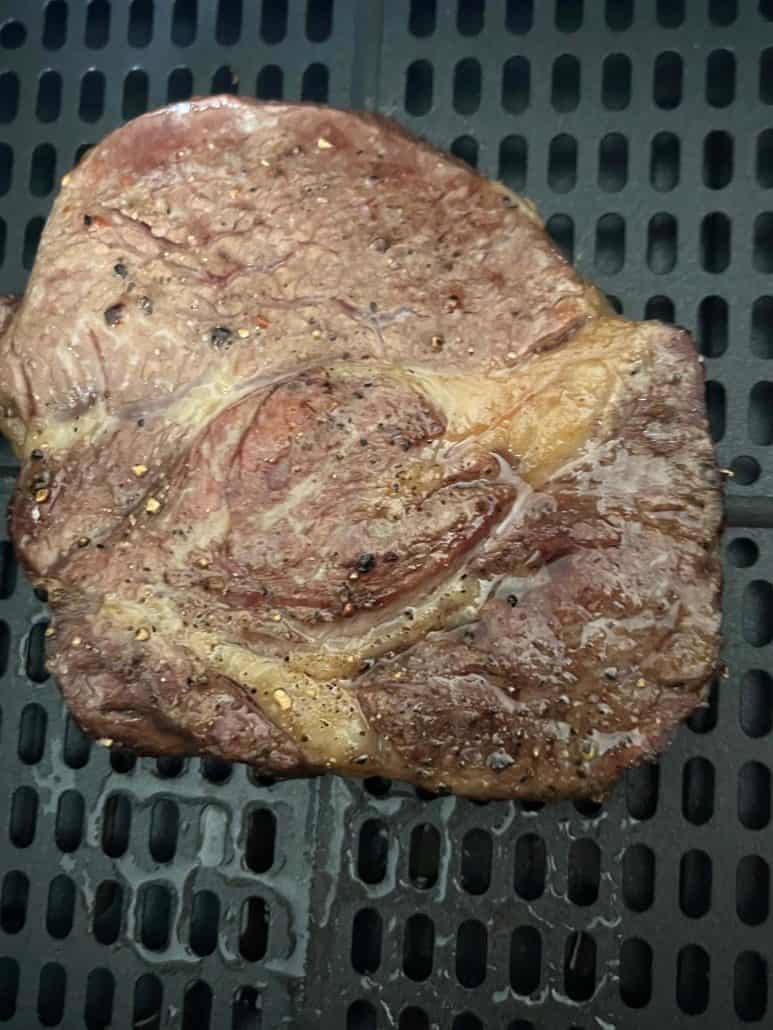 Close-up of cooked Delmonico steak in the air fryer basket, showing seared surface and juicy texture.