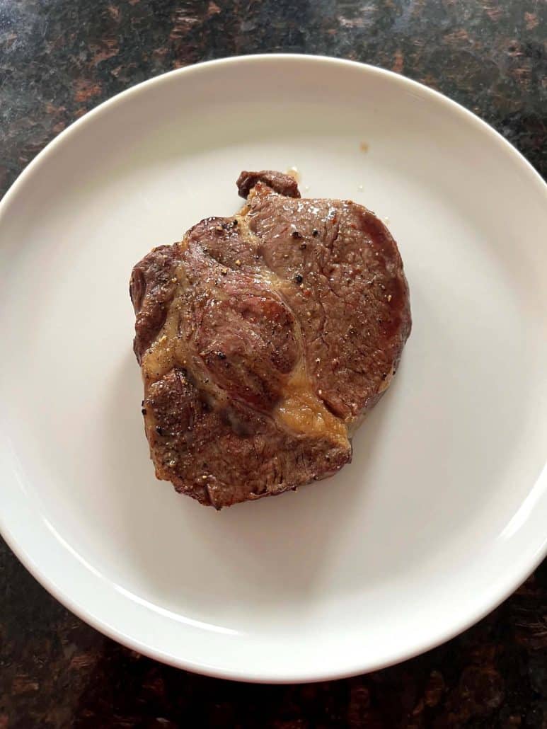 Cooked Delmonico steak resting on a white plate after air frying, ready to be sliced and served.