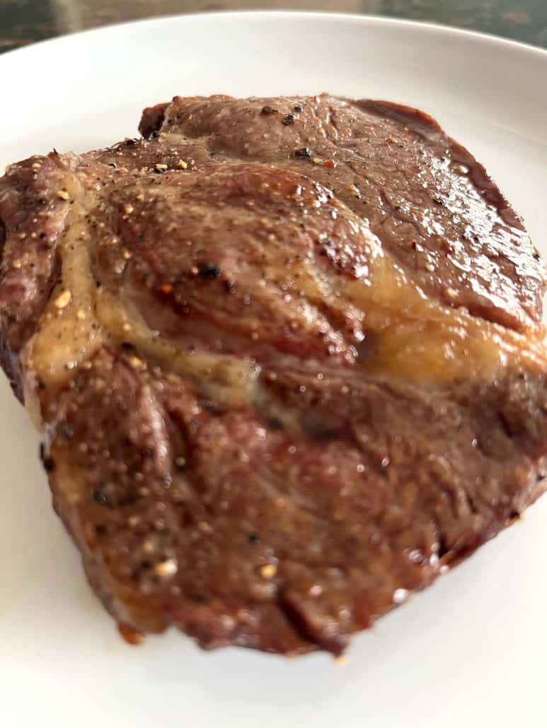 Air fried Delmonico steak resting on a white plate, showing caramelized edges and juicy, seared surface.