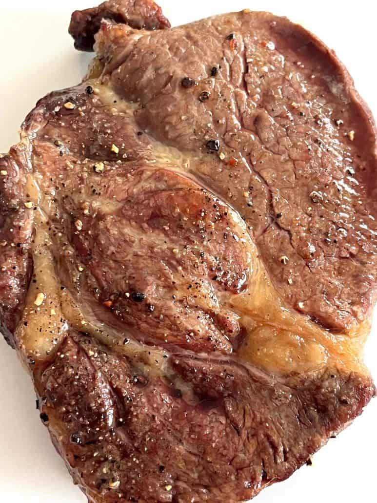 Whole air fried Delmonico steak on a white plate, cooked to perfection with a golden-brown sear.