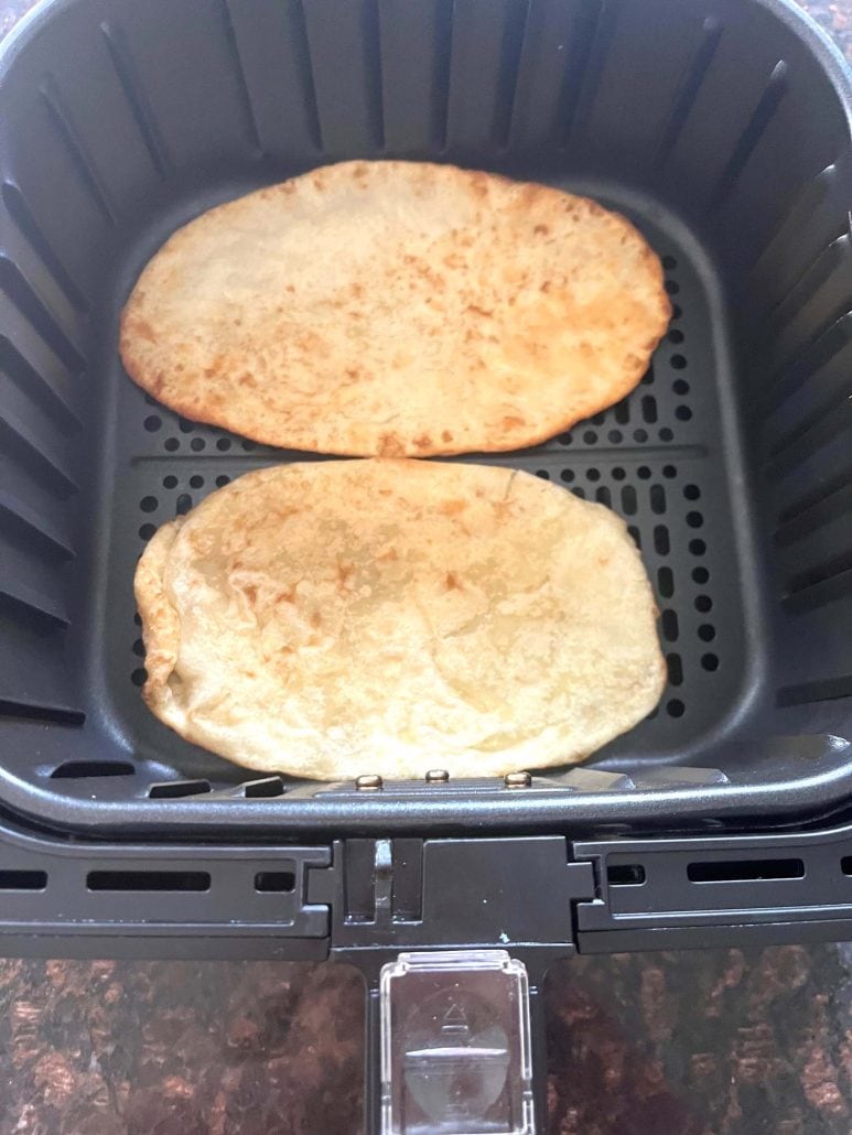 Two cooked bhatura in an air fryer basket—perfectly golden and puffed.