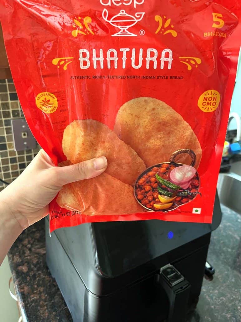 Hand holding a bag of frozen bhatura in front of an air fryer—getting ready to make quick and easy Indian flatbread.