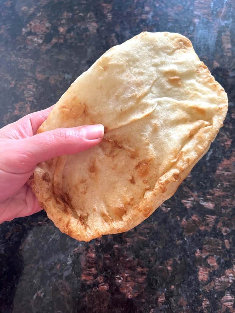 Hand holding a freshly air-fried bhatura—light, puffy, and golden brown, ready to enjoy.