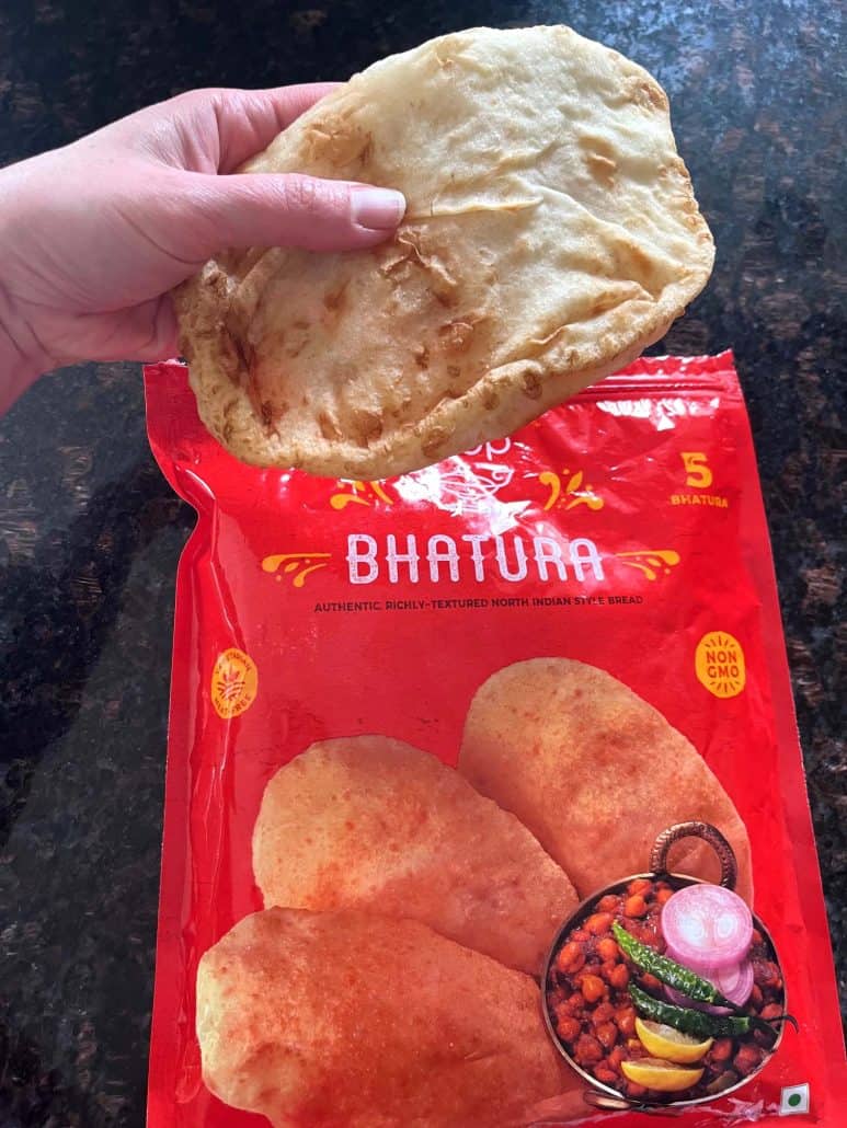 Hand holding a freshly air-fried bhatura over the original frozen packaging.