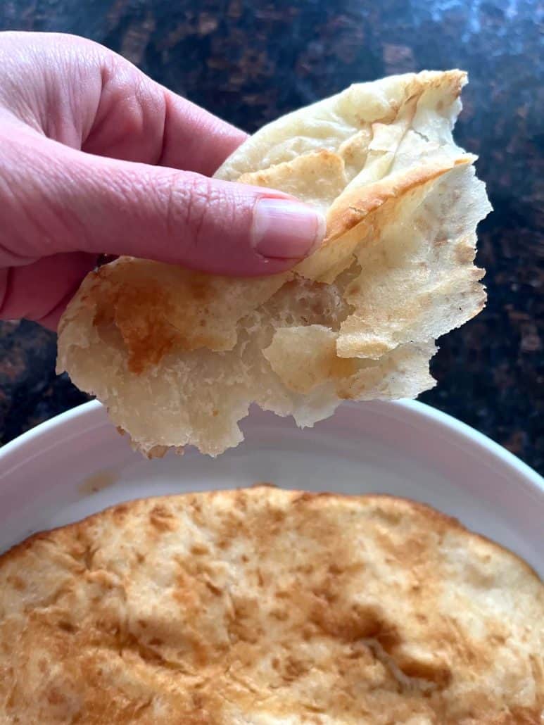 Close-up of a hand holding a torn piece of air-fried bhatura—showing its soft, fluffy interior and golden crispy edge.
