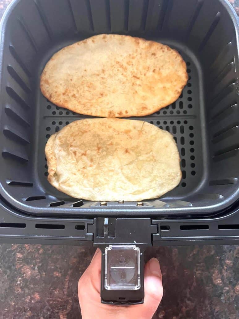 Two golden brown frozen bhatura breads cooking in an air fryer basket—perfectly puffed and ready in just 3 minutes using this easy air fryer method.