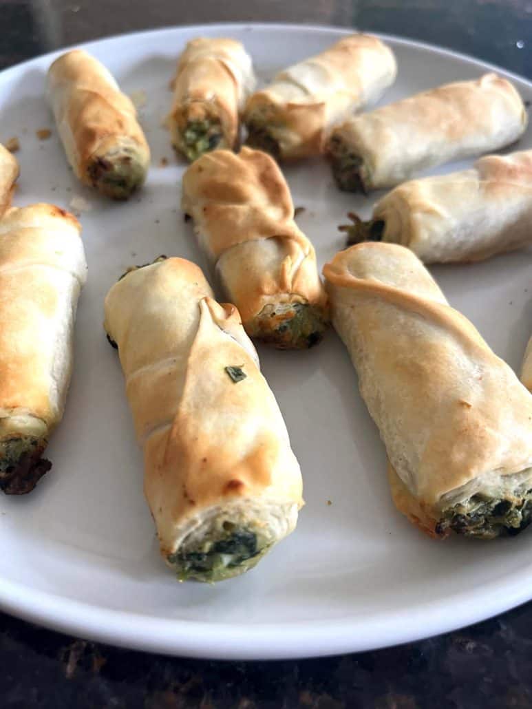 Side angle of air-fried borek bites on a white plate, showing the golden crispy layers and cheesy spinach filling.