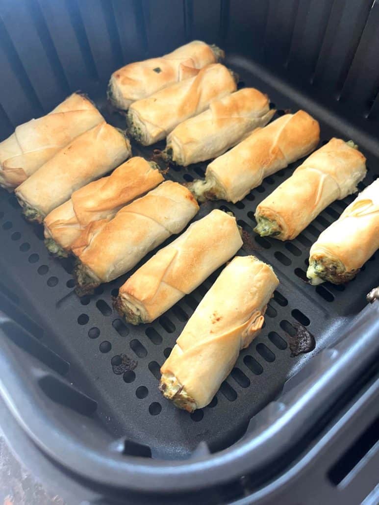 Side view of golden brown borek bites in an air fryer basket, perfectly cooked and ready to enjoy.