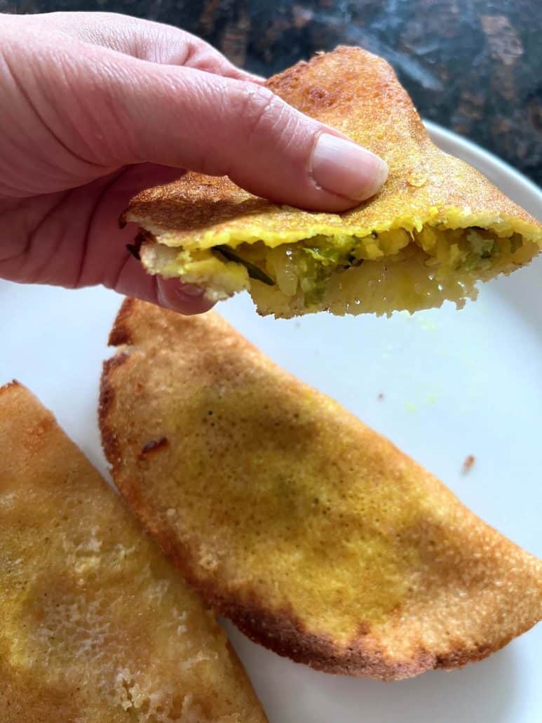 Hand holding a crispy air-fried masala dosa with a visible potato filling—showing the perfectly cooked center and golden crust.