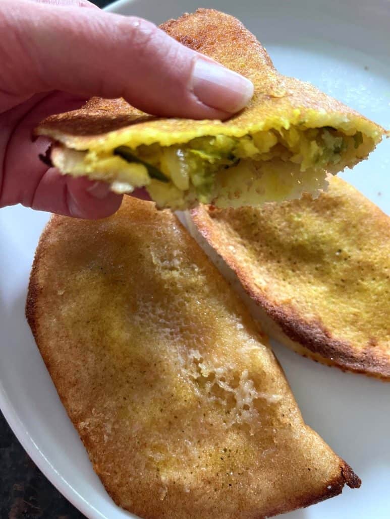 Close-up of a hand holding an air-fried masala dosa with spiced potato filling inside—highlighting the crispy edges and fully cooked center.