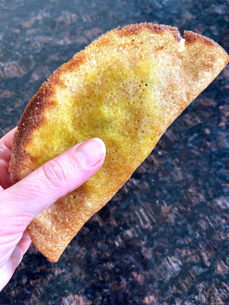 Hand holding a freshly air-fried masala dosa with a golden, crispy crust—ready to dip and enjoy.