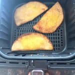 Three golden brown frozen masala dosas cooking in an air fryer basket—perfectly crisped using the no-preheat air fryer method.