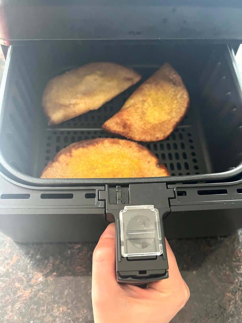 Hand pulling out air fryer basket with golden brown masala dosas freshly cooked.