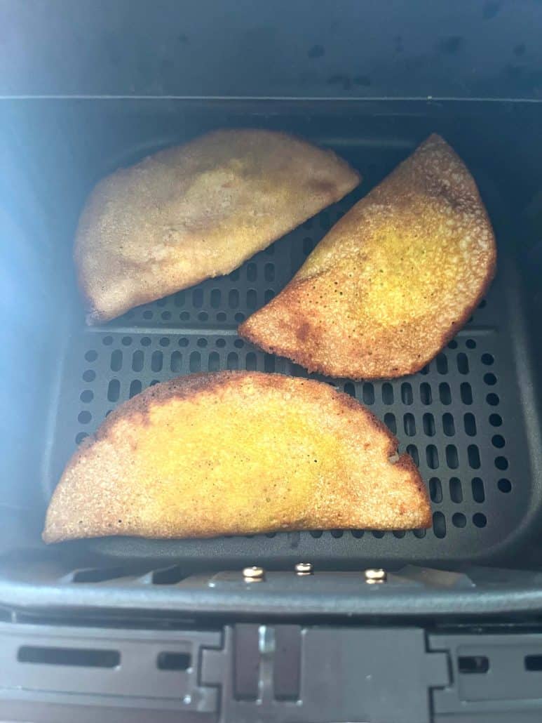 Three frozen masala dosas in an air fryer basket halfway through cooking.