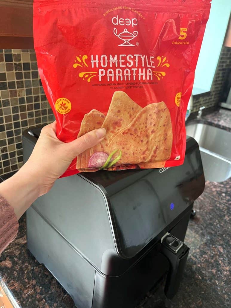 Holding a bag of frozen homestyle paratha in front of an air fryer—getting ready to cook this quick and easy Indian flatbread straight from the freezer.