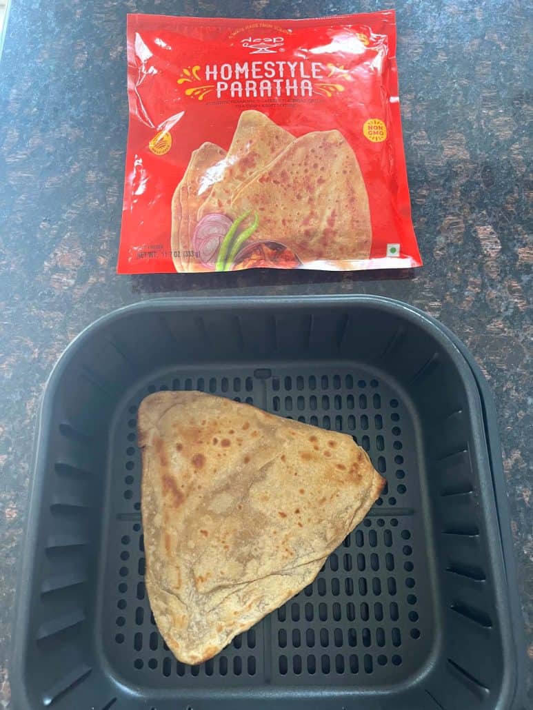 Frozen paratha placed in an air fryer basket with the packaging shown above—illustrating the brand and setup for this quick air fryer paratha recipe.