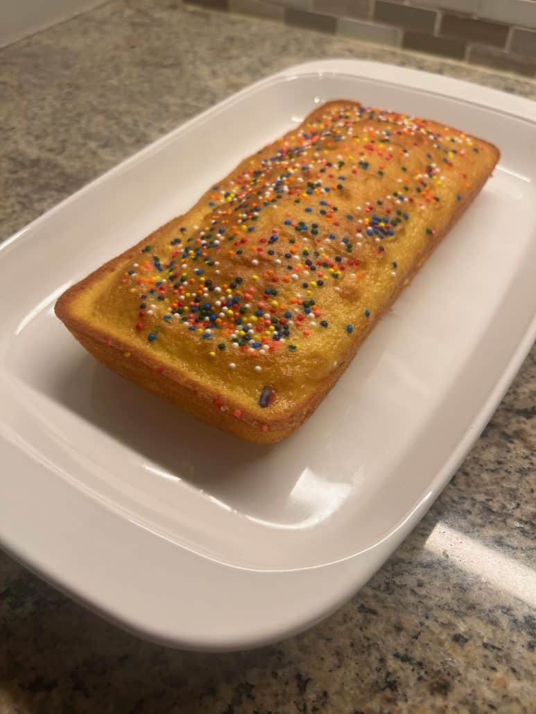 A close-up view of a freshly baked loaf cake with colorful sprinkles. Simple and delightful dessert made with 1 cup of cake mix.
