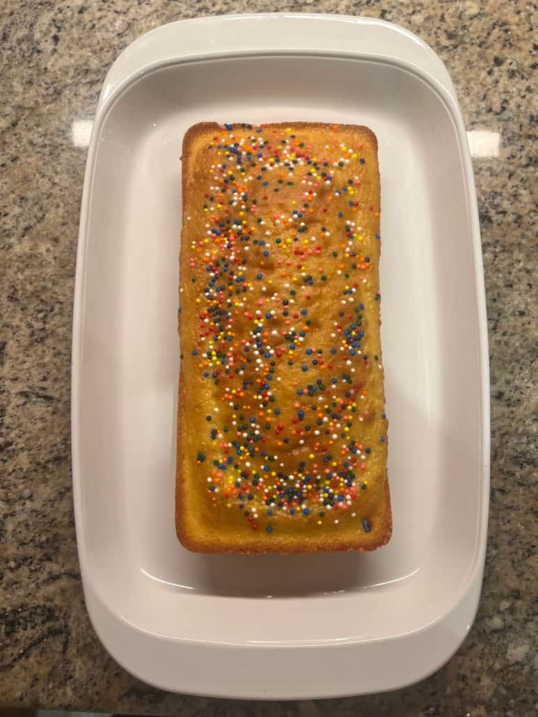 Top view of a freshly baked loaf of cake with colorful sprinkles, placed on a white platter, showcasing a fun and easy dessert made with 1 cup of cake mix.