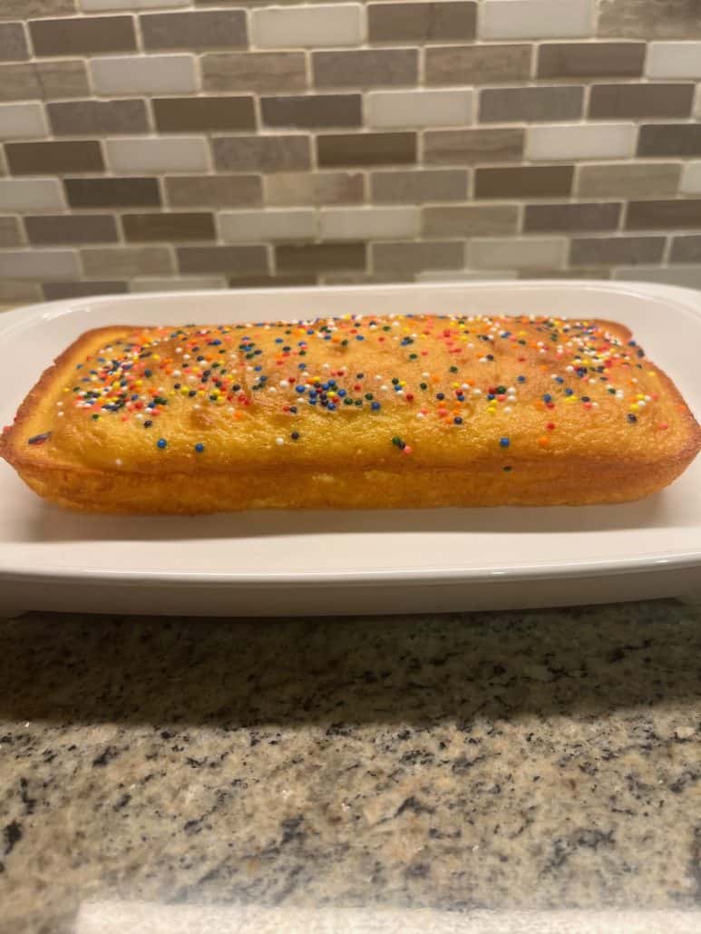 Side view of a colorful sprinkles-topped loaf cake, resting on a white platter.