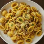 A white plate filled with one-pan orecchiette pasta tossed with browned sausage, Parmesan cheese, and fresh parsley.