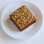A slice of Texas Sheet Cake topped with chopped walnuts on a white plate, showing the fudgy icing and moist texture.