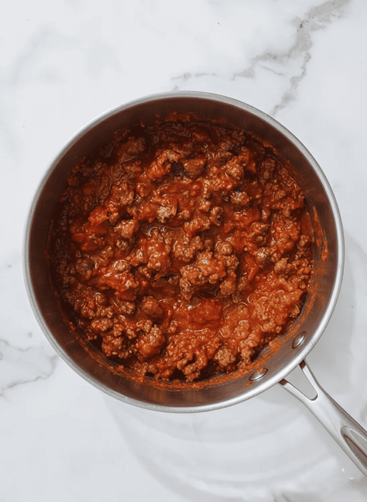 A pot of simmering meat sauce, rich in color with chunks of tomato and ground meat, ready to be layered in the baked spaghetti dish.