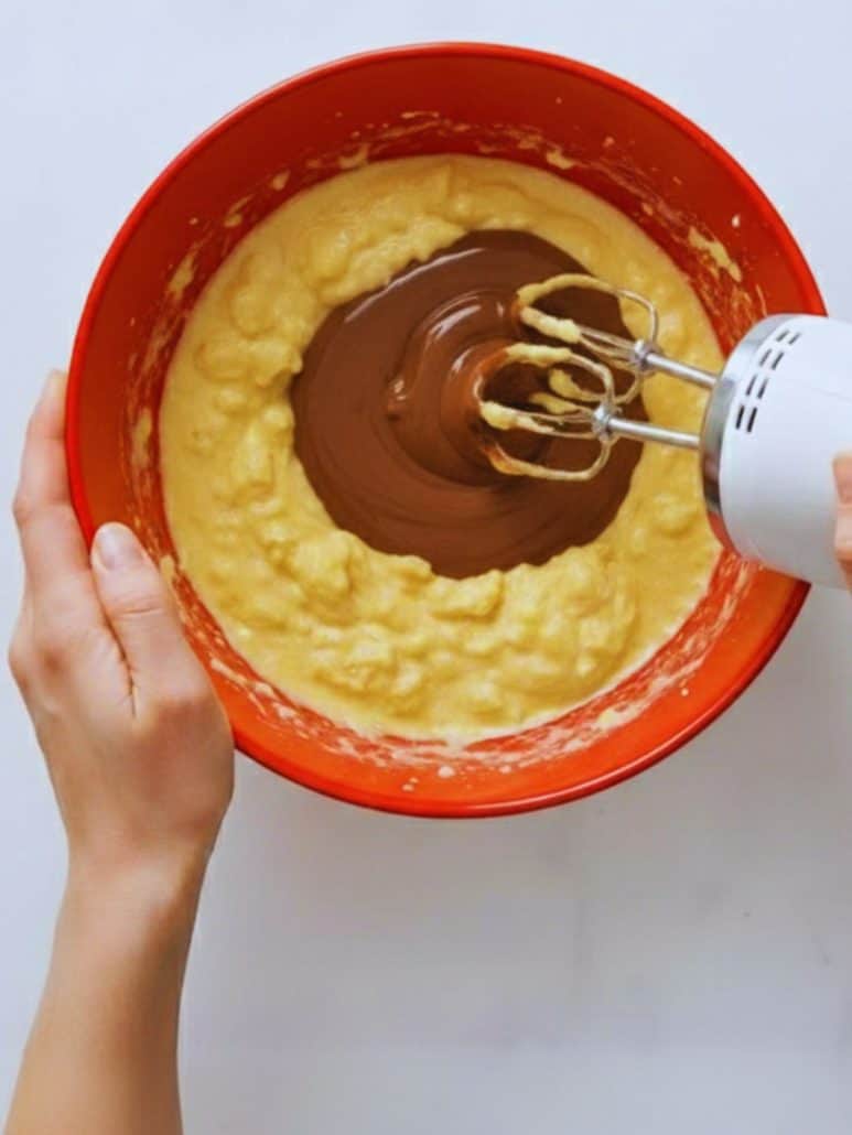 Mixing the Texas Sheet Cake batter in a red bowl, with melted chocolate being blended into the egg and sour cream mixture.