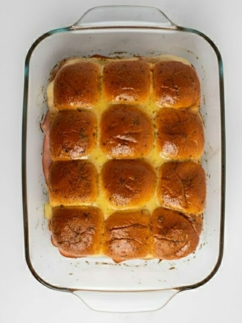 Freshly baked ham and cheese sliders in a glass dish with golden, buttery tops, just out of the oven.