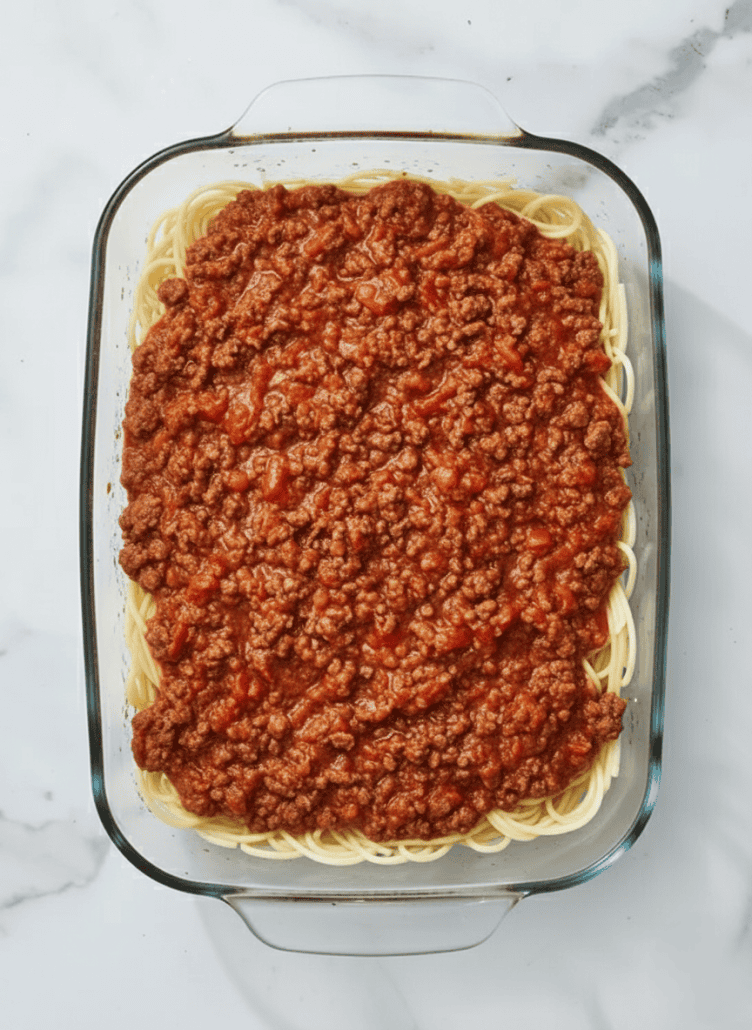 A layer of savory meat sauce spread over the cooked spaghetti, ready to be topped with cheese and baked into a delicious casserole.