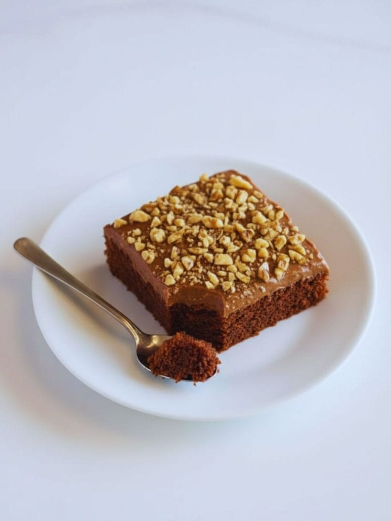 A single serving of Texas Sheet Cake topped with chopped walnuts on a white plate.