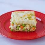 Slice of viral TikTok chicken cobbler on a red plate showing layers of creamy chicken, peas, carrots, and golden biscuit topping.