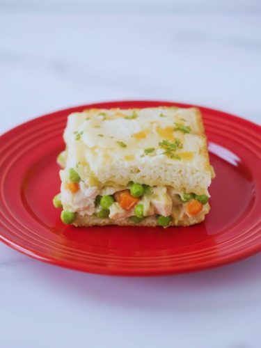 TikTok Chicken Cobbler Recipe With Red Lobster Biscuit Mix Slice of viral TikTok chicken cobbler on a red plate showing layers of creamy chicken, peas, carrots, and golden biscuit topping.