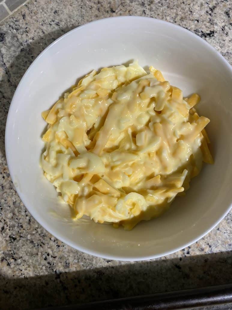 Cheese mixture made with shredded cheddar, egg, mayo, and garlic in a white bowl.