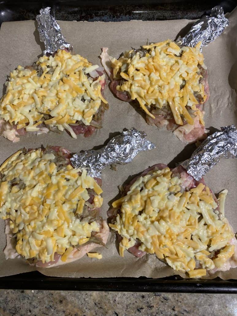 Unbaked chicken thighs on a sheet pan topped with shredded potato, onion, and cheese mixture. Final prep before baking Cheesy Baked Chicken Thighs With Bone In.