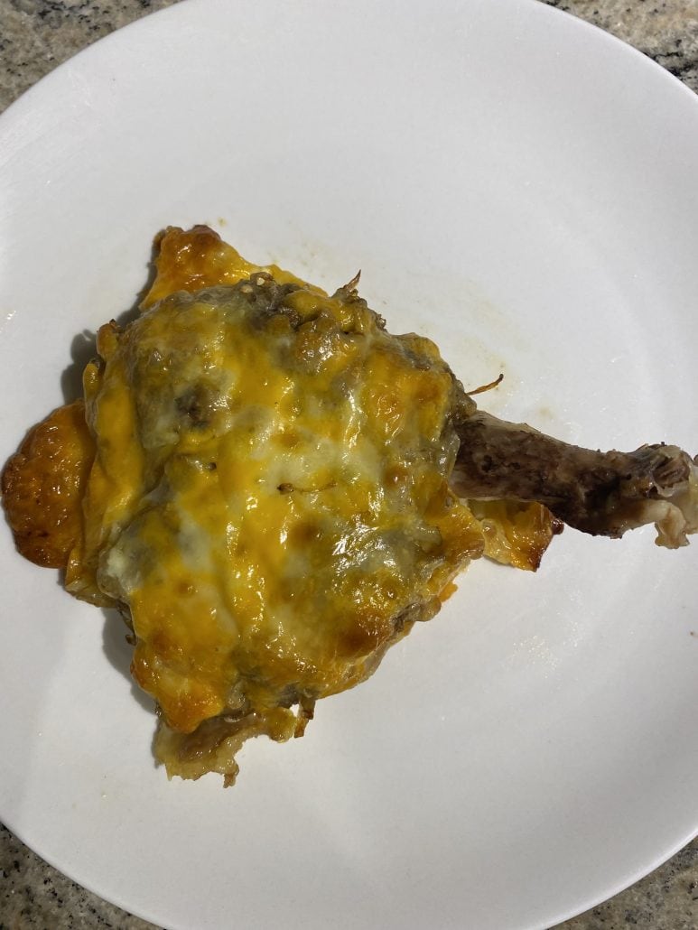 Close-up of one fully baked cheesy chicken thigh with golden melted topping on a white plate.