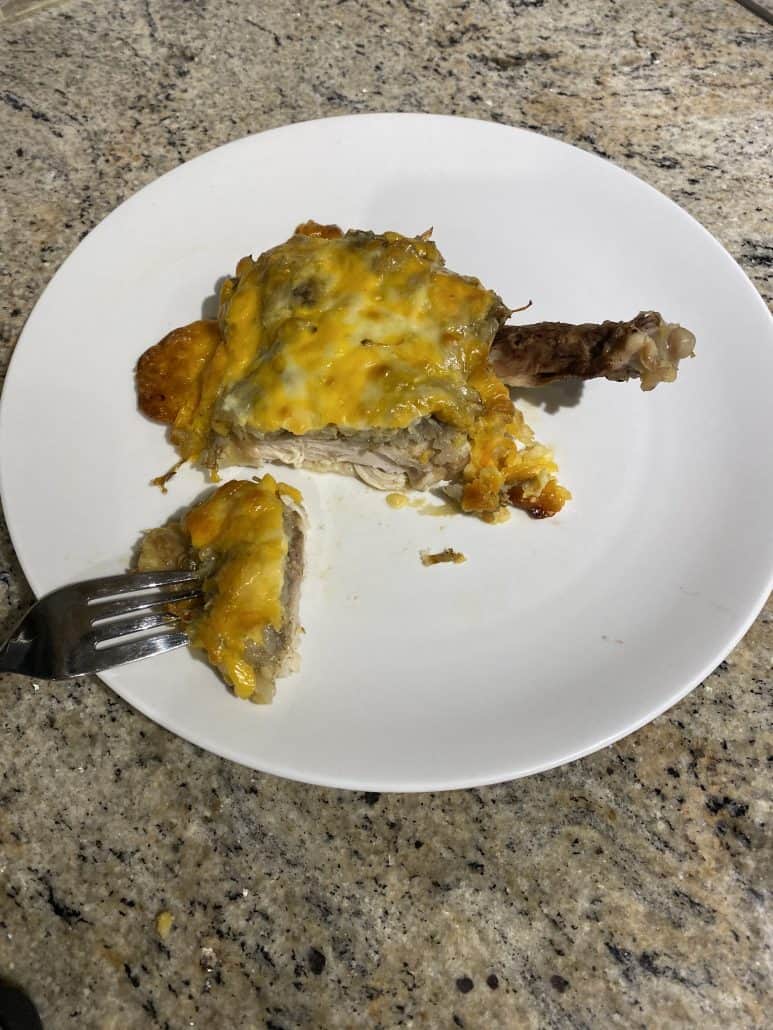 Cheesy baked chicken thigh on a white plate with a fork cutting into a juicy slice.