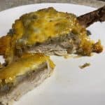 Cheesy baked chicken thigh topped with golden melted cheese and potato mixture, served on a white plate.