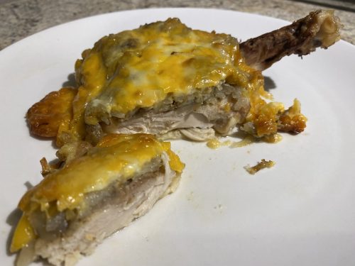 Tender Cheesy Baked Bone-In Chicken Thighs Recipe Cheesy baked chicken thigh topped with golden melted cheese and potato mixture, served on a white plate.