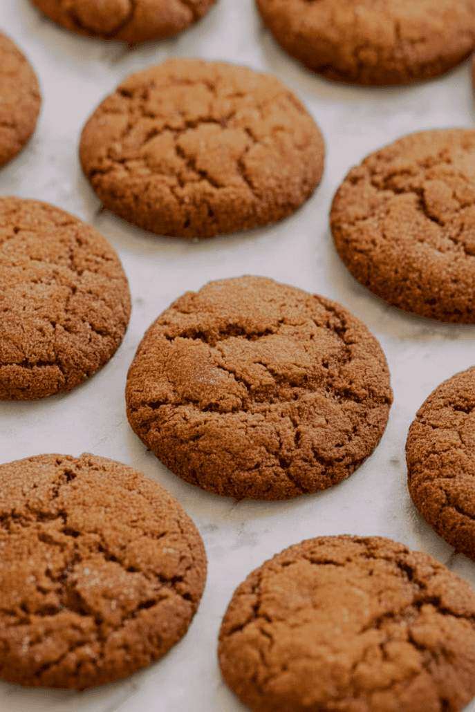 Freshly baked gingersnap cookies cooling on parchment paper, showcasing their crackled tops and chewy texture straight from the oven.