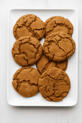 Soft and chewy gingersnap cookies with crackled tops arranged on a white rectangular plate – the perfect homemade holiday treat.