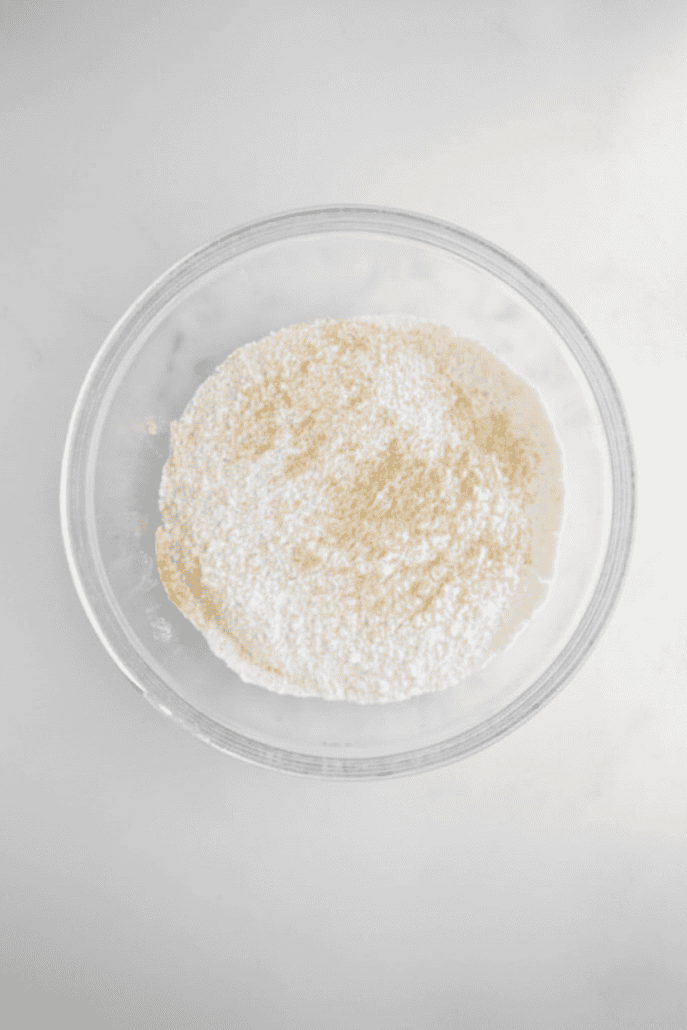 Dry ingredients for gingersnap cookies—flour, spices, and baking soda—sifted together in a clear mixing bowl.