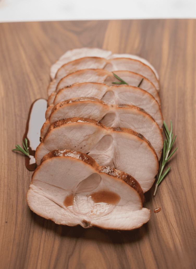 Sliced honey pineapple glazed ham arranged on a wooden cutting board with rosemary, ready to serve as featured in the holiday ham recipe.