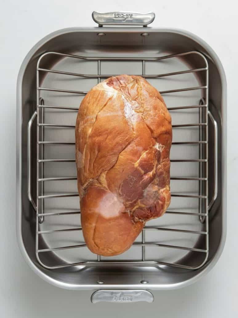 Unbaked bone-in ham placed on a rack inside a roasting pan, ready to be cooked for the honey glazed ham recipe.