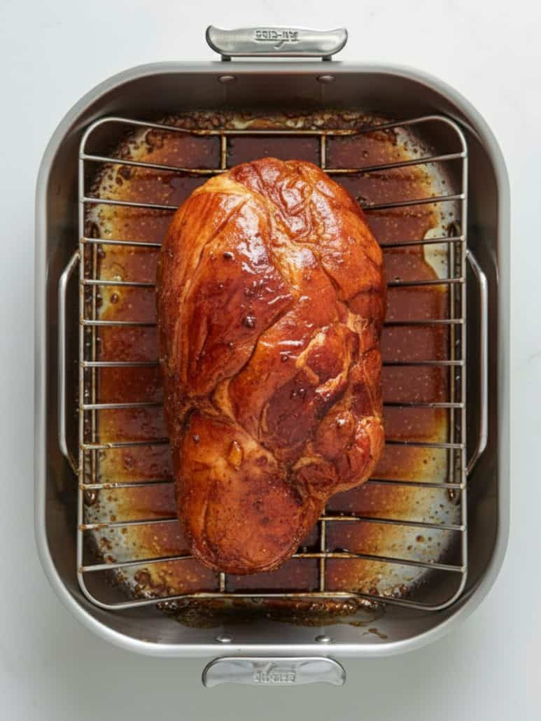 Glazed ham baking in a roasting pan, caramelized with layers of pineapple honey glaze.