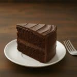 Slice of rich, moist one bowl chocolate cake with chocolate chip frosting, served on a white plate.