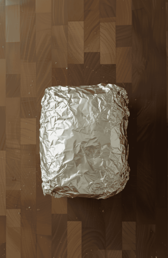 Cooked prime rib roast wrapped in foil and resting—an essential step to keep the meat juicy and tender before slicing.